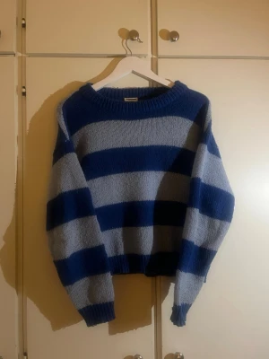 Randig blå stickad tröja Noisy May - Säljer en oversized stickad tröja från Noisy May i storlek M. Tröjan har breda horisontella ränder i mörkblått och ljusblått, rund hals och långa ärmar. Perfekt för dig som gillar chill och avslappnad stil.