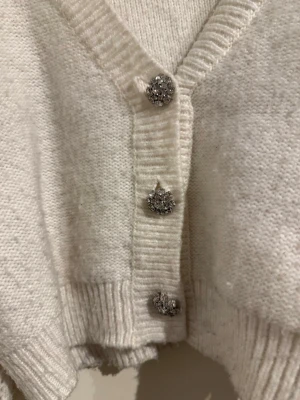 Stickad vit kofta från Gina  - Tröjan har fina silvriga knappar men är lite nopprig, det går troligtvis bort med en klädborste.