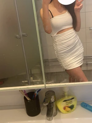 Vit omlott kortklänning med cut-out - Säljer en vit, tight kortklänning med omlott-design och snygg cut-out vid midjan. Klänningen har oneshoulder och är rynkad längs sidorna för en cool effekt. Perfekt för dig som gillar trendiga och stilrena plagg med lite edge.