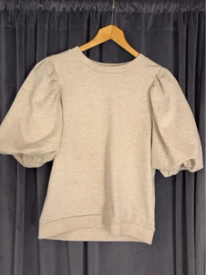 Beige topp med puffärm - Säljer en beige topp från Kappahl i storlek XS. Toppen har rund halsringning och stora puffärmar som ger en cool och trendig look. Andvända ej längre, topp skick!!