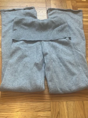 Grå stickade mjukisbyxor med ribbad midja - Säljer ett par grå stickade mjukisbyxor med bred ribbad midja. Byxorna har en loose passform och är perfekta för chill dagar. Materialet är mjukt och stretchigt, vilket gör dem superbekväma. Passar dig som gillar avslappnad stil och vill ha något riktigt comfy.