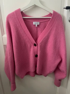 Rosa kofta från & Other Stories XS - Superfin rosa kofta från & Other Stories i storlek XS. Koftan är ribbstickad med v-ringning och har tre svarta knappar framtill. Modellen är loose fit med långa ärmar och breda muddar. Perfekt att slänga på sig för en chill look.