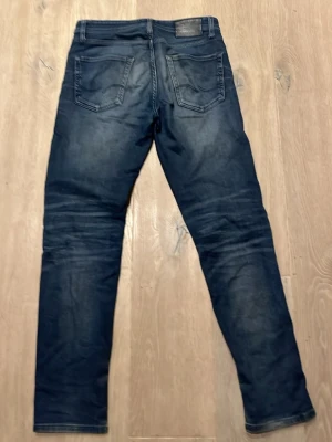 Jack & Jones Tapered Mike jeans blå 29/32 - Snygga blå jeans från Jack & Jones, modell Tapered Mike. De har en tapered passform med klassiska fem fickor och coola slitningar. Jeansen är tillverkade i jeansmaterial och har normal midja. Perfekt för dig som gillar en modern och avslappnad stil.