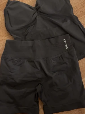 Grått träningsset från DFYNE - Säljer ett grått träningsset från DFYNE med sport-bh och matchande shorts. Setet är gjort i mjukt och stretchigt syntetmaterial som sitter skönt mot kroppen. Både toppen och shortsen har logotypen tryckt framtill och bred ribbad midja för extra support.