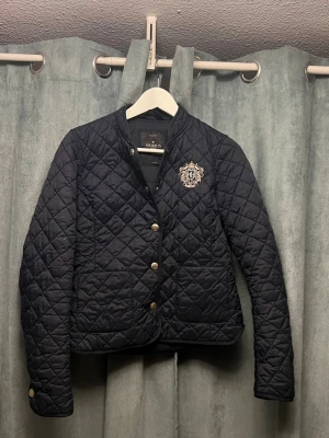 Morris jacka  - Quiltad mörkblå jacka från Morris med silverfärgade knappar och broderad emblem. Perfekt för dig som gillar klassisk och snygg stil. Passar xs/s