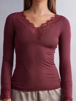 Vinröd intimissimi topp med spets - Säljer en vinröd långärmad topp från Intimissimi med v-ringad hals och dekorativ spets både vid halsringningen och ärmsluten. Modellen är slim och har en mjuk, stretchig känsla. 