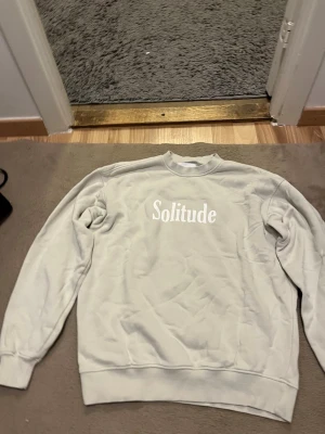 Beige sweatshirt Solitude från Vailent - Säljer en beige sweatshirt från Vailent i storlek S med trycket 'Solitude' i vitt på bröstet. Tröjan har rund hals, ribbade muddar och är långärmad. Mjuk insida som känns skön mot huden, perfekt för chill dagar.
