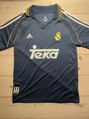 Real Madrid 1998/99 vintage Adidas tredje fotbollströja - En mörkblå retro Real Madrid fotbollströja från Adidas i storlek M, med gulddetaljer och Aeroready-material. Väldigt bra skick!