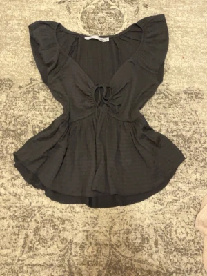 Svart blus med volang och knyt - Säljer en svart blus från 157 med snygga volangärmar och knyt framtill. Blusen har en feminin v-ringning och är tillverkad i ett lätt, mjukt material som ger ett fint fall. Perfekt att styla med jeans eller kjol för en trendig look.