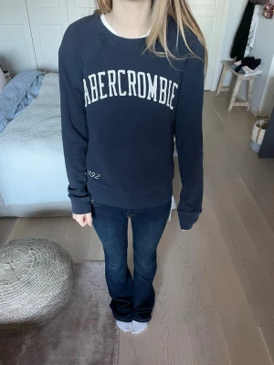 Mörkblå sweatshirt från Abercrombie - Säljer en mörkblå sweatshirt från Abercrombie & Fitch i storlek S. Tröjan har vit text framtill, rund hals och långa ärmar. Mjuk bomullskänsla och klassisk passform, perfekt för chill dagar. Snyggt tryck med Abercrombie och årtal 1892 på framsidan.