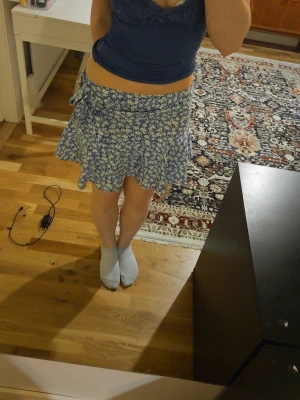 Blå vit blommig kjol - Säljer en blå,vit blommig kjol med inbyggda shorts och ett avtagbart knytsnöre