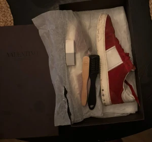 Valentino Garavani röda sneakers - Säljer ett par snygga Valentino flycrews som är i fint skick. Det ingår skor, box och mocka sudd. Hör av er vid frågor!! Obs det har varit två hål framme vid skon på båda skorna på ena sidan, men allt är fixat så allt sitter ihop med hjälp av lim.