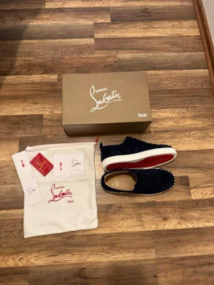 Mörkblå Christian Louboutin skor - Snygga mörkblå sneakers från Christian Louboutin i mocka med ikoniska röda sulor och coola nitar framtill. Skorna har snörning och vit platt sula. Perfekt för dig som vill sticka ut med exklusiv design och detaljer. De är testade en gång och är i utmärkt skick. Fick precis hem de i en haul men de passade inte så därför säljer jag de!   Skriv i dm om ni har några frågor!