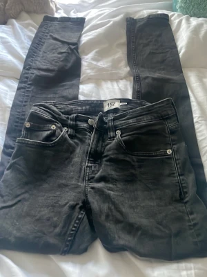 Svarta jeansbyxor från 157, XS - Svarta jeansbyxor från 157 i storlek XS. Klassisk femficksmodell med silverfärgade nitar och knapp. Byxorna har en rak passform och är tillverkade i ett slitstarkt jeanstyg som ger en cool och enkel look. Perfekt för dig som gillar stilrena svarta jeans.