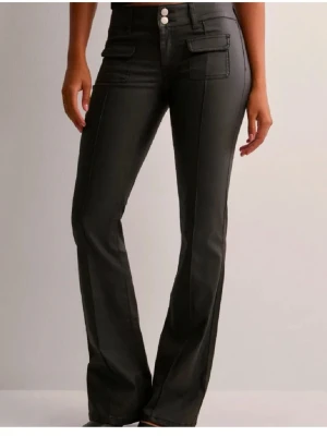 Svarta bootcut byxor Nelly - Snygga svarta skinn byxor med bootcut passform. Byxorna har dekorativa ficklock framtill och dubbla knappar i midjan. Materialet ser ut att vara bomull eller polyester med en lätt glansig finish. Perfekta för en trendig och stilren look.