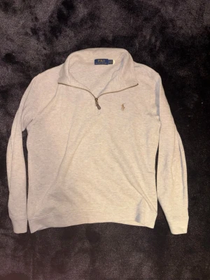 Ljusgrå half zip från Polo Ralph Lauren - Säljer en ljusgrå långärmad tröja från Polo Ralph Lauren med klassisk broderad logga på bröstet. Tröjan har en snygg half zip-dragkedja och hög krage. Perfekt för chill höst- och vinterdagar. Materialet är mjukt och känns som bomull.