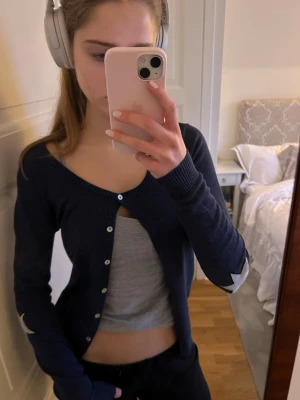 Mörkblå kofta med stjärndetaljer - Säljer en mörkblå kofta med rund halsringning och vita knappar. Koftan har långa ärmar och coola ljusgrå stjärnor på armbågarna.