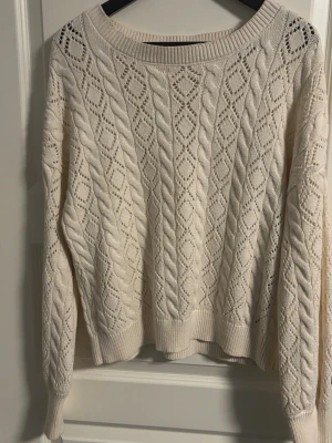 Stickad vit tröja  - Säljer en vit stickad tröja i storlek L. Tröjan har ett snyggt kabelstickat mönster med håldetaljer.