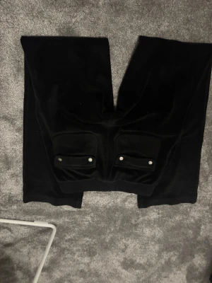 Svarta mjukisbyxor Juicy Couture XXS - Svarta mjukisbyxor från Juicy Couture i storlek XXS. Byxorna har bred resår med snörning i midjan (bara ett snöre går att dra i det andra är fast i byxorna), två fickor baktill med silverfärgade knappar och broderad JC-logga på ena fram fickan. Mjukt material som känns lyxigt och chill. Priset kan ändras🤗