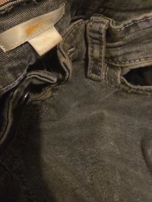 Grå jeansbyxor från Gina Tricot - Säljer ett par grå jeansbyxor från Gina Tricot i storlek 164. Byxorna har klassisk femficksdesign med snygga detaljer på bakfickorna och bälteshällor. Materialet är jeans och färgen är en tvättad grå ton som ger en cool vibe.