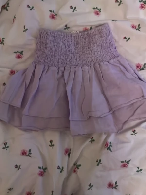 Ljuslila volangkjol från Zara - Supersöt ljuslila kortkjol från Zara med bred smock i midjan och dubbla lager volanger. Den är ganska tajt i midjan men passar mig som är 164. Använts ett par gånger