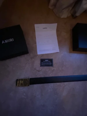 Svart skinnbälte från Amiri - Säljer ett stilrent svart bälte från Amiri med en fet guldfärgad logotyp som spänne. Bältet är gjort i skinn och kommer med originalbox och certifikat. Perfekt för dig som vill ha en lyxig och edgy detalj till outfiten.