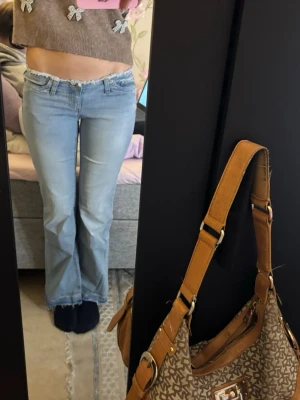 Bootcut ljusblå jeans med fransad kant - Säljer ett par ljusblå bootcut jeans med låg midja och fransad kant längst ner då den är uppsprättad. Jeansen har klassisk femficksdesign och är tillverkade i mjukt denimtyg. Passformen är bootcut och de har en snygg, avslappnad vibe. Perfekta för dig som gillar retrostil och vill ha något bekvämt.
