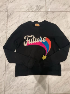 Svart kashmirtröja från From Future - Svart stickad tröja i 100% kashmir från From Future med färgglad framtidsinspirerad design på bröstet. Trycket har texten 'Future' och en stjärna med rosa, blå och röd båge. Rund hals och långa ärmar, perfekt för dig som gillar coola statement-plagg.