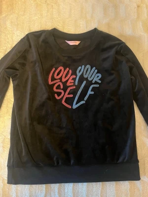 Svart velourtröja Hunkemöller S - Svart långärmad tröja från Hunkemöller i mjuk velour med broderad text 'LOVE YOURSELF' i rött och blått framtill. Tröjan är SUPERSKÖN.  Rund halsringning och ribbade muddar vid ärmslut och nederkant. Perfekt för chill dagar och snygg att styla med jeans.