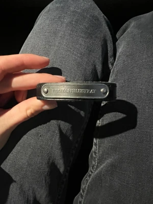 Svart läderarmband Marc Jacobs - Snyggt svart läderarmband från Marc Jacobs med metallplatta där det står 'VERITAS INLUSTRAT'. Armbandet har tryckknapp och detaljer i silverfärgad metall. Perfekt accessoar för att ge din outfit en cool och stilren touch. Storlek S de bild 5, nypris 550 kr 