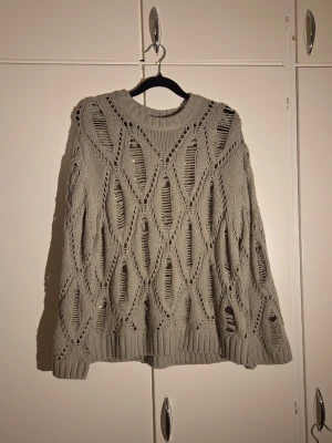 Khaki stickad tröja från H&M Divided - Säljer en stickad tröja från H&M Divided i storlek S. Tröjan har ett öppet, hålmönstrat design med breda ribbade muddar vid ärmslut och nederkant. Materialet är 100% akryl och modellen är loose fit med långärmade ärmar. Perfekt för lager-på-lager under hösten.