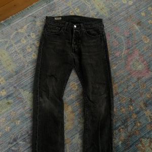 Levi's 501 svarta jeans, straight fit - Svarta Levi's 501 Premium jeans med klassisk straight fit och knappgylf. Jeansen har fem fickor, diskret sliten look och är tillverkade i robust bomullsdenim. Passar dig som gillar tidlös stil och vill ha ett par jeans som funkar till allt.