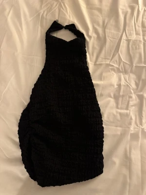 Svart smockad halterneck topp Zara - Säljer en svart smockad halterneck topp från Zara i storlek S. Toppen har en åtsittande passform med knyt runt nacken och är ärmlös. Perfekt till sommaren och enkel att styla med både jeans och kjol.