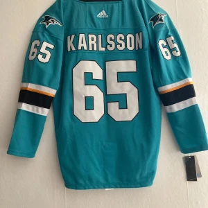 Erik Karlsson #65 NHL tröja - Säljer en NHL-matchtröja från svenska stjärnbacken Erik Karlsson med #65 på ryggen. Tröjan är från tiden när han spelade i San Jose Sharks.   •Storlek: 52 (motsvarar L/XL) • “This is Sharks Territory” i kragen • NHL-logo framtill • Snörning i halsen • Fight strap (knapp inuti tröjan för att fästa i byxorna) Tröjan har bara hängt på väggen sedan jag köpte den  och priset kan diskuteras bara att slänga iväg ett meddelande.