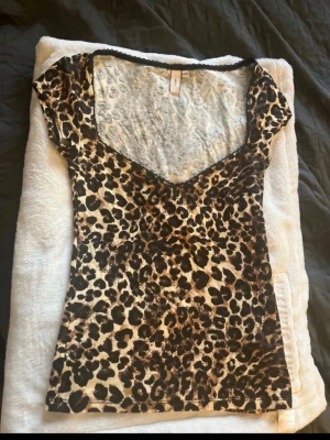 Leopardmönstrad topp från Nelly XXS - Säljer en kortärmad topp från Nelly i storlek XXS med leopardmönster i bruna och svarta toner. Toppen har v-ringad hals med svart spetskant och är figurnära i modellen. Perfekt för dig som gillar djurmönster och vill sticka ut.