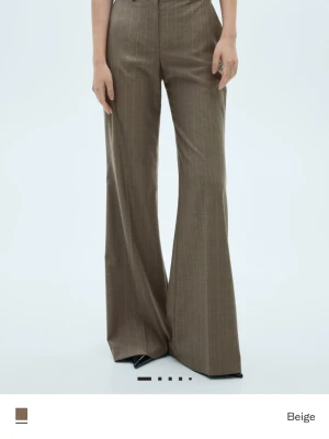 Mango kritstrecksrandiga kostymbyxor - Snygga beige kostymbyxor med diskret randigt mönster och breda ben. Byxorna har hög midja och dragkedja fram. Materialet känns som en blandning av bomull och polyester, perfekt för en clean och modern look.