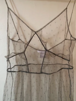 Svart prickig meshklänning från H&M - Säljer en lång transparent meshklänning från H&M i svart med tunna axelband och prickigt mönster. Klänningen har markerade sömmar och v-ringad front, perfekt för att styla lager på lager. Supersnygg och trendig look!