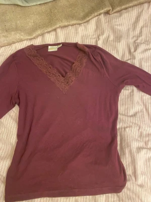 Vinröd långärmad topp Gina Tricot - Säljer en vinröd långärmad topp från Gina Tricot med v-ringning och spetsdetalj runt halsen. Toppens material är mjukt och stretchigt, perfekt för dig som gillar enkel men snygg stil. Passar dig som vill ha en basic topp med lite extra detalj.