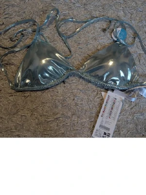 Bikini-topp - Säljer en bikini-topp i färgen icy blue. Toppen har trekantsformade kupor och tunna knytband både i nacken och runt ryggen. Perfekt för strandhäng och bad under sommaren.