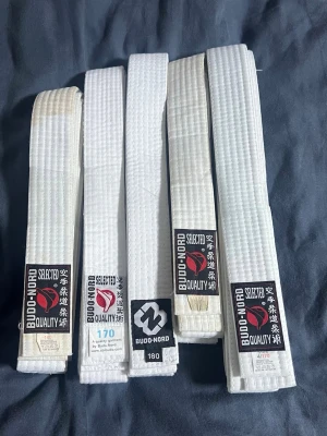 Vita karate bälten - Bilderna visar fem vita budobälten från Budo-Nord i olika storlekar, tillverkade av bomull och polyester. Inga skor syns på bilderna.