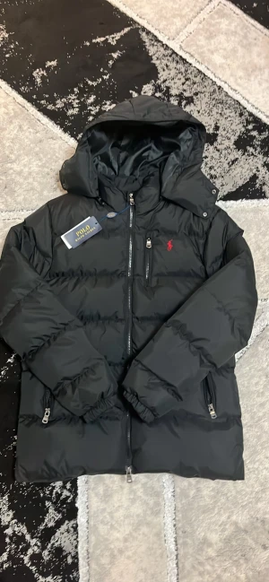 Svart pufferjacka från Polo Ralph Lauren - Svart pufferjacka från Polo Ralph Lauren med röd broderad logga på bröstet. Jackan är i storlek S och är lite stor i storleken. Pris går att diskuteras 
