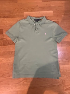 Grön piké från Polo Ralph Lauren - Snygg ljusgrön pikétröja från Polo Ralph Lauren i slim fit-modell. Klassisk krage, korta ärmar och tre knappar framtill. Ikoniska broderade loggan i vitt på bröstet. Perfekt för dig som gillar stilrena och tidlösa plagg. Skick helt ny.