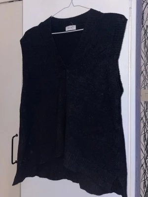 Svart stickad väst från Mix by - Svart stickad väst från Mix by med v-ringad hals och ribbade kanter. Modellen är loose fit och har en enkel, stilren design utan mönster eller extra detaljer. Perfekt att slänga över en skjorta eller t-shirt för en chill look.