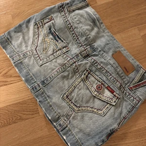 Jeanskjol från ONLY, storlek 36 - Säljer en snygg ljusblå jeanskjol från ONLY i storlek 36. Kjolen har coola detaljer som dubbla knappar fram, kontrastsömmar i rött och flera fickor med dekorativa sömmar. Perfekt för dig som gillar en avslappnad och trendig stil.