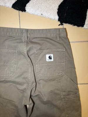 Carhartt cargopants i beige bomull - Ett par Carhartt carpenter byxor i bra skick!  Strl 25. Midja: 72cm Längd: 103  Hör gärna av dig om du undrar något eller vill ha fler bilder! ✌🏻