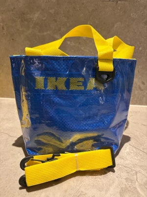 Blå axelväska från IKEA med gul rem - LIMITED EDITION! Säljer en ikonisk blå axelväska från IKEA med tydlig logga och starka gula handtag samt avtagbar axelrem. Axelrem ingår. Helt oanvänd.  Inte tillverkad av Ikea