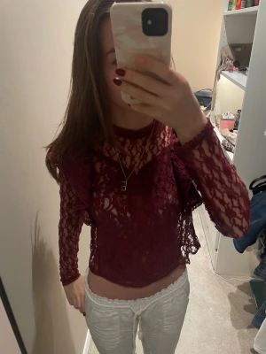 Vinröd spetsblus med volangdetaljer - Säljer en vinröd blus i spets med långärmade ärmar och snygga volangdetaljer på axlarna. Blusen är genomskinlig. Perfekt för dig som gillar att sticka ut med detaljer och färg. Tröjan är från NA-KD och är i stolek 32! Skriv såklart till mig ifall du har några frågor eller funderingar!💕