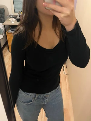 Svart långärmad topp med v-ringning - Säljer en svart långärmad topp med v-ringad hals. Toppen har en slim passform och är gjord i mjukt bomullsmaterial som sitter skönt mot kroppen. Perfekt att matcha med jeans eller kjol för en enkel och stilren look.