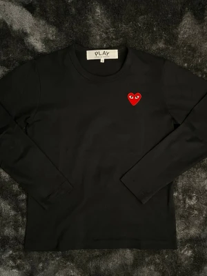 Svart långärmad t-shirt Comme des Garçons - Svart cdg long sleeve med det ikoniska röda hjärtat med ögon broderat på bröstet. Storlek S men är lite mindre i storleken så sitter ungefär som en XS.