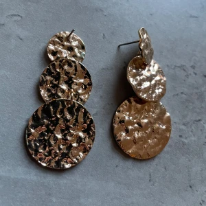 Guldfärgade örhängen  - Stora, cirkelformade örhängen i guld med hamrad yta. Plopp saknas men passar med vilka som helst som jag har haft. 